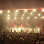 Gösterişli kostümler ve sahne ışıkları altında performans sergileyen rock grubu