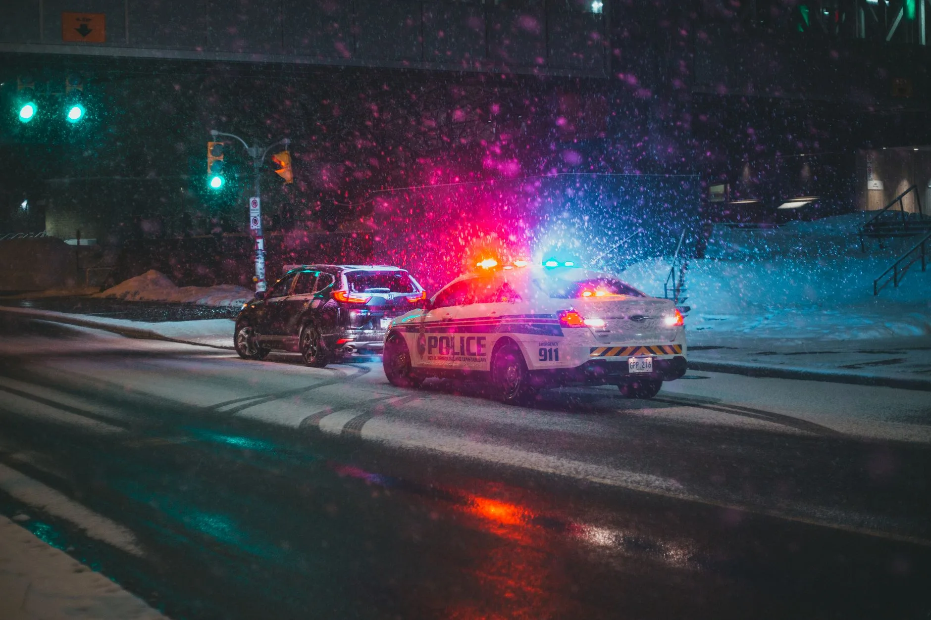Gece kar yağışı altında polis ışıklarıyla aydınlanan yol